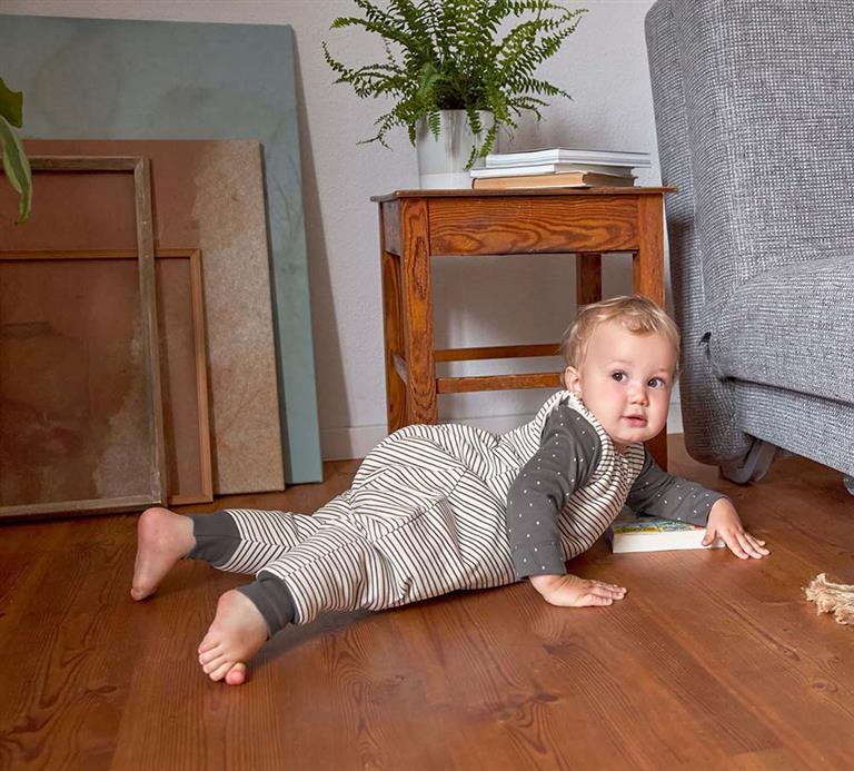 Bebé a gatinhar no chão de madeira, vestindo o saco de dormir com pernas Lassig TOG 2,5 antracite, ideal para brincar.
