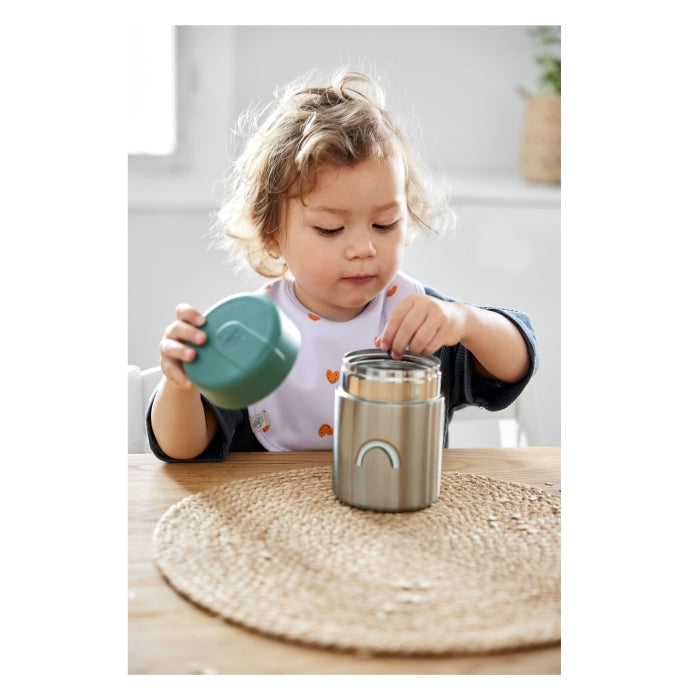 Criança pequena a usar o termo Lassig 315ml Smile Green na mesa, ideal para refeições fora de casa.