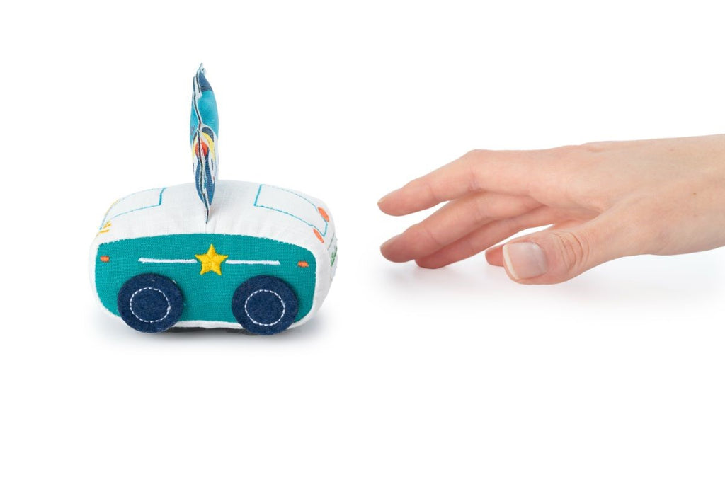 Mão alcançando carrinho de tecido Lilliputiens polícia branco e azul. Mostra interação com brinquedo para bebé.