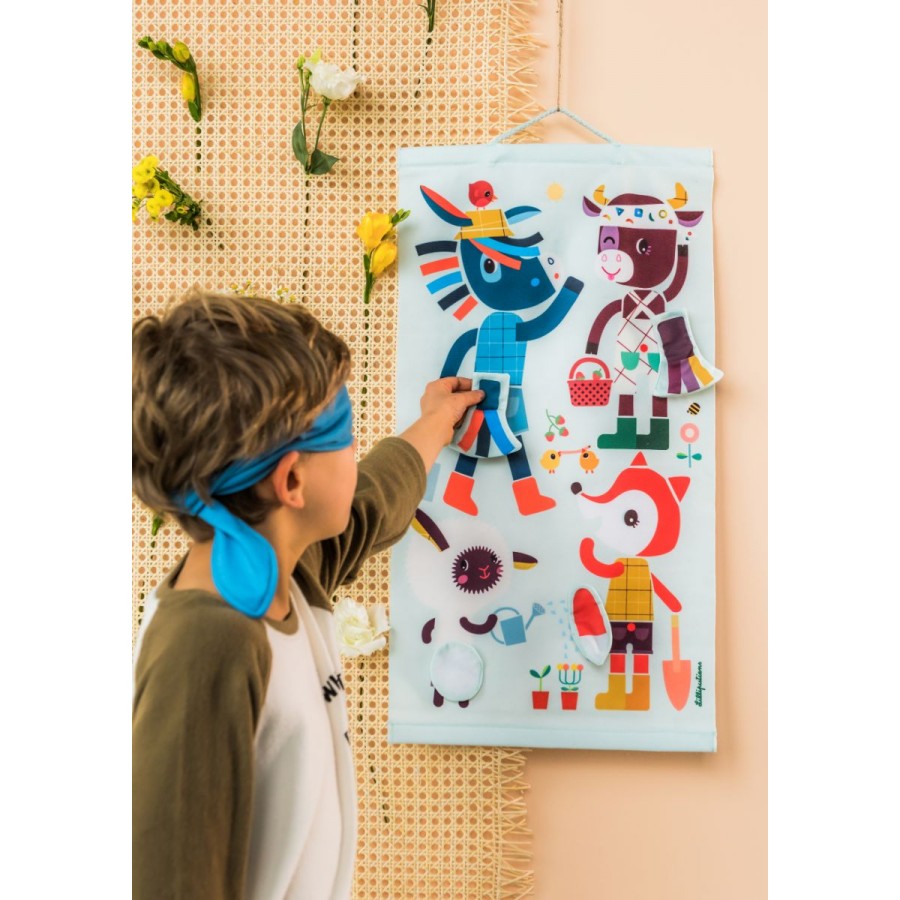 Criança de olhos vendados a tentar colocar uma cauda no burro do jogo de orientação Lilliputiens pendurado na parede.