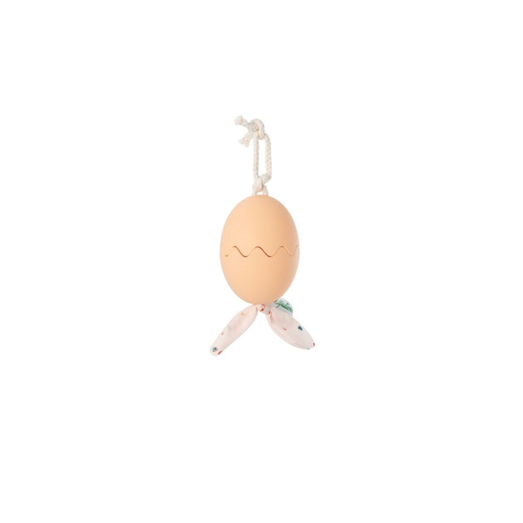 Ovo de brinquedo Lilliputiens fechado, cor pêssego, com corda para pendurar e tecido estampado visível na base.