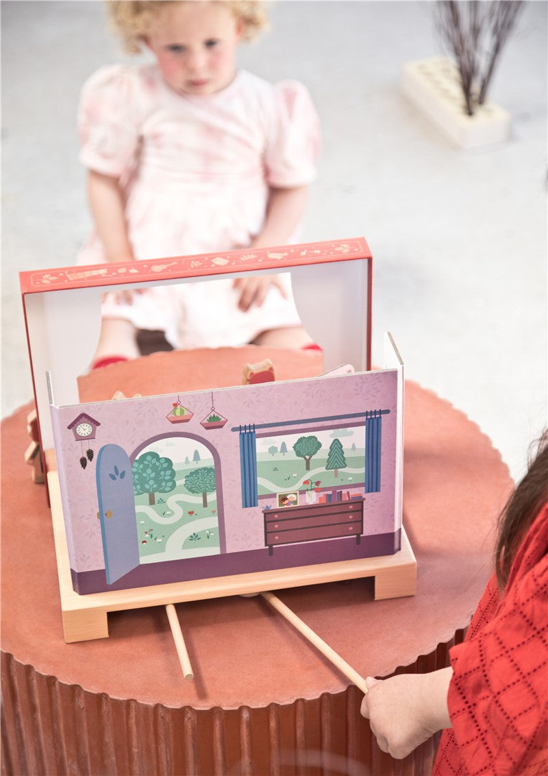Crianças a brincar com o teatro magnético Lilliputiens montado com cenário interior, numa mesa redonda.