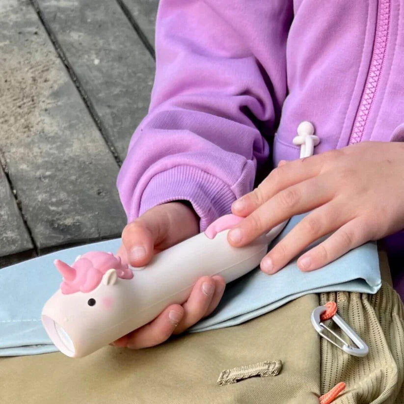 Detalhe das mãos de uma criança a segurar a Lanterna silicone Pinky da Rabbit & Friends, enfatizando o design ergonómico e o material suave.