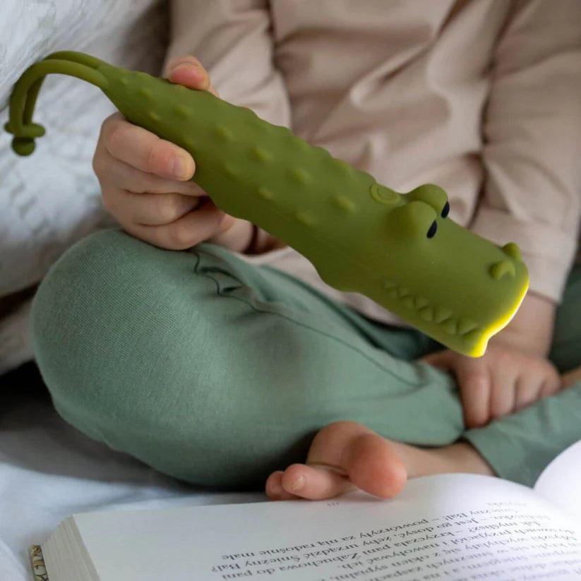 Criança a usar a lanterna Rabbit & Friends Croco em silicone verde para ler um livro na cama.