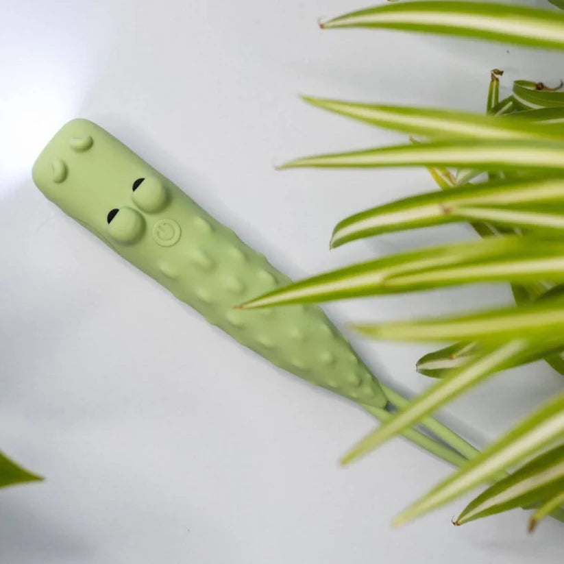 Lanterna Rabbit & Friends Croco em silicone verde, vista superior, com botão e olhos, junto a folhagem.