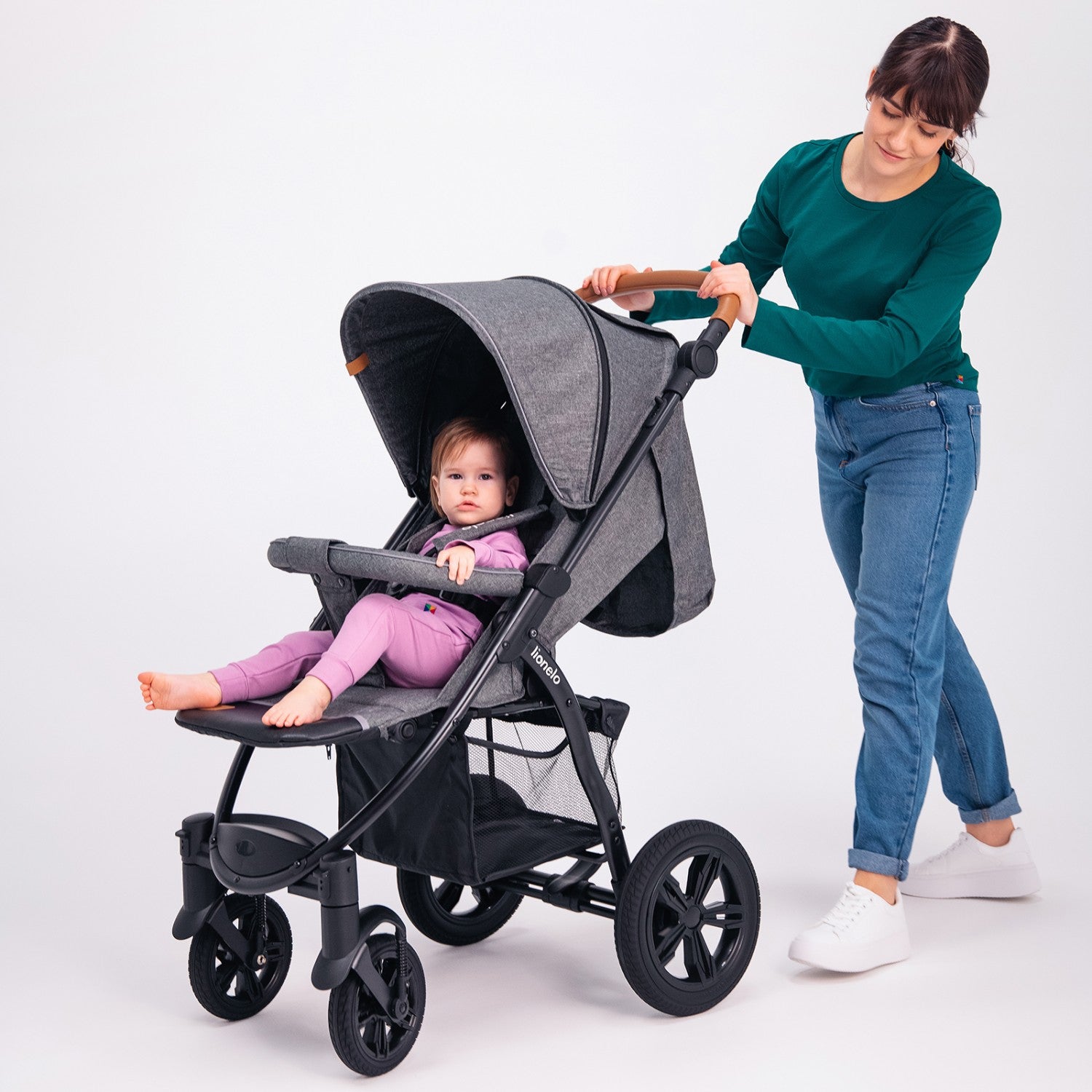 Mãe empurra o carrinho de passeio Lionelo Annet Tour cinzento com um bebé sentado, destacando o guiador ajustável e o cesto de arrumação.