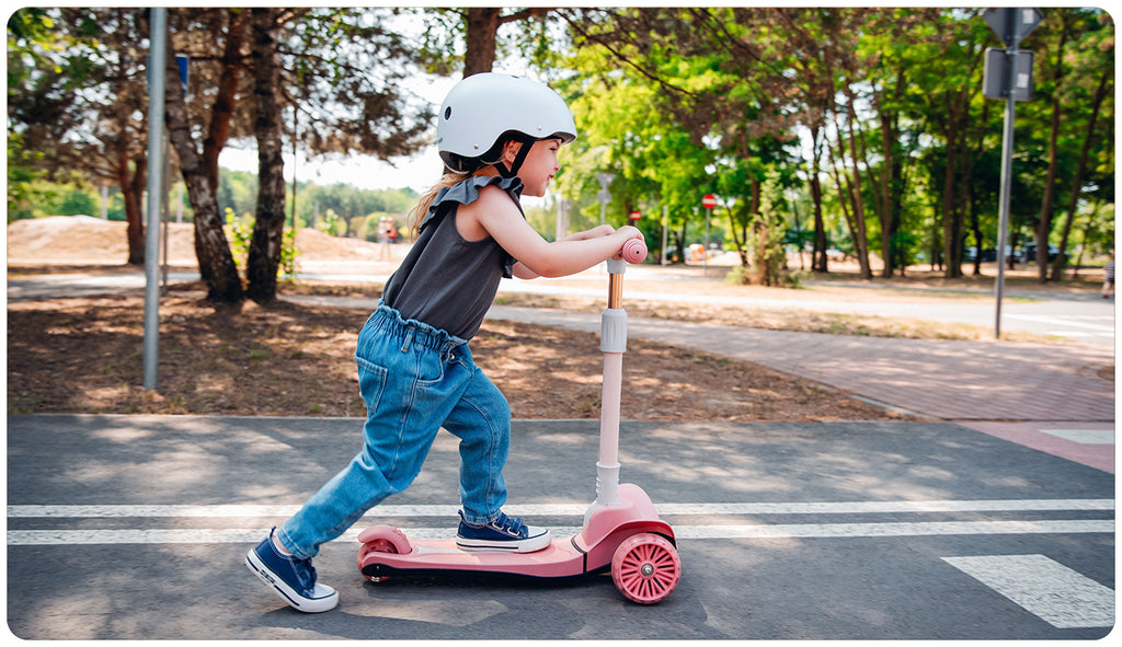 Criança a usar a trotinete de 3 rodas Lionelo Timmy cor-de-rosa num passeio, demonstrando estabilidade e diversão ao ar livre.