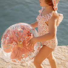 Criança com fato de banho a segurar a bola de praia 3D Little Dutch junto ao mar.