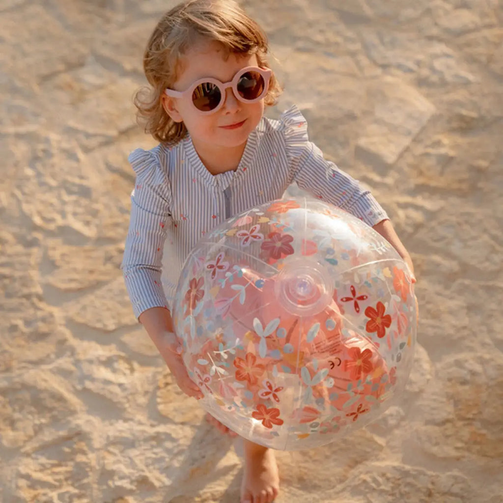 Criança com óculos de sol a segurar a bola de praia 3D Little Dutch de flores.