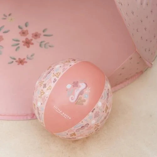 Detalhe da Bola de Praia Little Dutch cor-de-rosa com padrão de cavalos-marinhos e algas, perto de um tecido rosa.