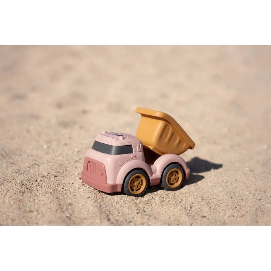 Camião de reboque Little Dutch cor-de-rosa na areia da praia, com foco no brinquedo e no ambiente arenoso.