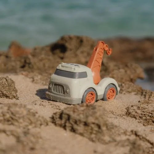 Camião de reboque Little Dutch bege e laranja, com rodas grandes, posicionado sobre a areia da praia perto da água.