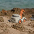 Camião de reboque Little Dutch bege e laranja, com rodas grandes, posicionado sobre a areia da praia perto da água.
