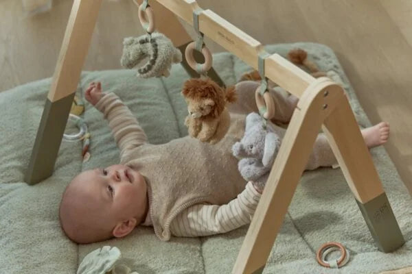 Bebé deitado a brincar com os peluches suspensos do ginásio de madeira Safari Friends da Little Dutch.