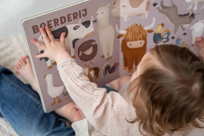 Visão aérea de uma criança pequena a interagir com a página de animais da quinta ("Boerderij") do livro de cartão Little Dutch.