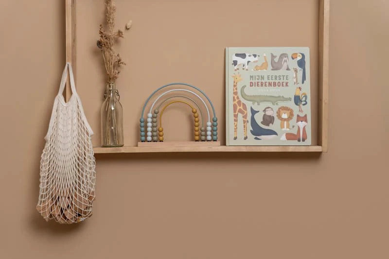 Livro "Mijn Eerste Dierenboek" da Little Dutch em exposição numa prateleira de madeira, ao lado de um ábaco arco-íris e um saco de rede.