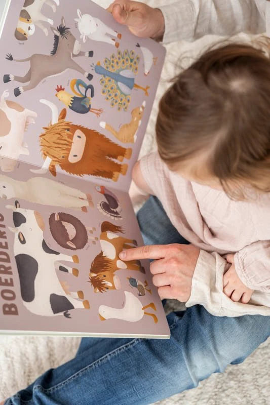 Pai e criança a lerem o livro Little Dutch sobre animais da quinta, com o dedo da criança a apontar para uma vaca e um cavalo.