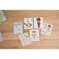 Vista aérea de vários livros de atividades Little Dutch, incluindo o Dress Me Up, abertos sobre uma superfície de madeira, mostrando diferentes temas e autocolantes.