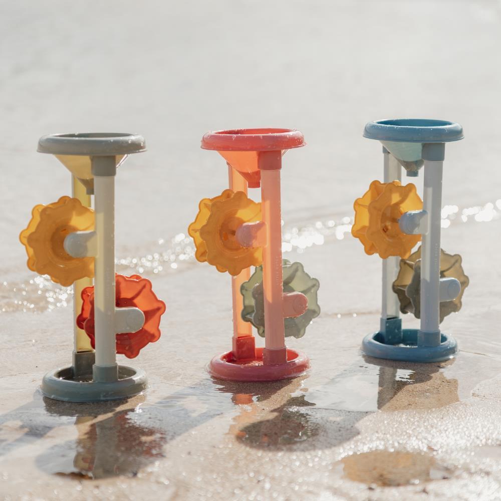 Três moinhos de areia e água Little Dutch em cores pastel (cinza, rosa e azul) alinhados na areia molhada junto à água do mar.
