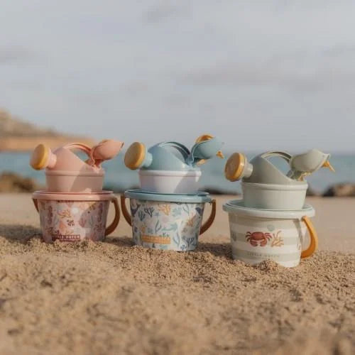 Três conjuntos de praia Little Dutch Ocean Dreams (rosa, azul e verde) com balde, regador e acessórios, dispostos na areia da praia.