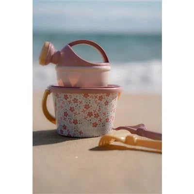 Conjunto de praia Little Dutch rosa sobre a areia com o mar desfocado ao fundo, ideal para brincar junto à água.