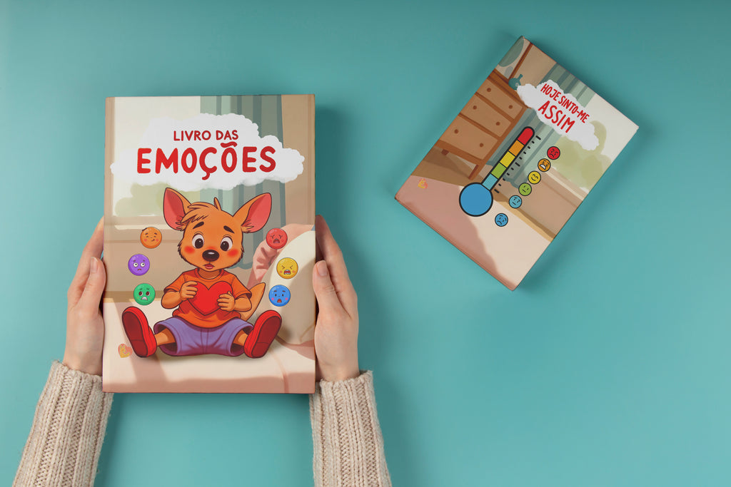 Duas mãos seguram o livro físico "Livro das Emoções" com o Moki a abraçar um coração, ao lado de um termómetro de emoções "Hoje sinto-me assim" sobre fundo azul-turquesa.