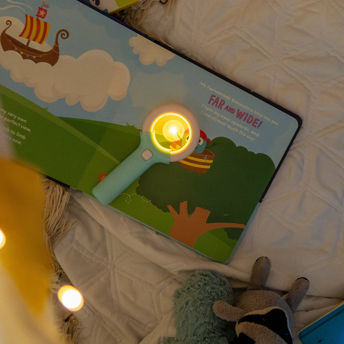 Livro aberto com a Varinha Mágica GloPals a iluminar uma página que descreve binóculos feitos em casa para ver longe e alto.