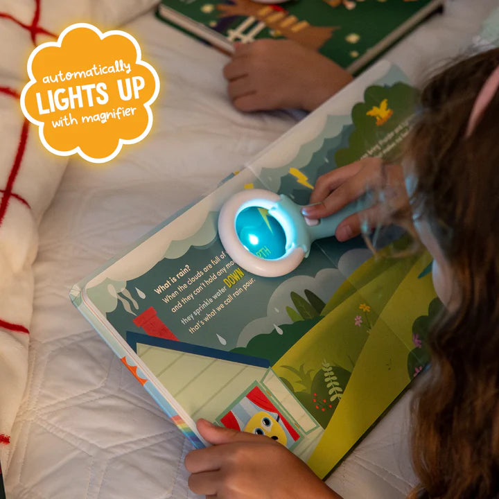 Criança a usar a lupa mágica que ilumina o livro "What is rain?" da Glo Pals, demonstrando a funcionalidade de luz automática para ler o texto sobre a chuva.