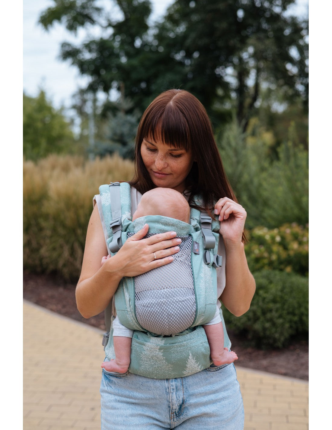 Mulher a usar a mochila Love and Carry ONE, com o bebé à frente, ao ar livre, com vegetação ao fundo.