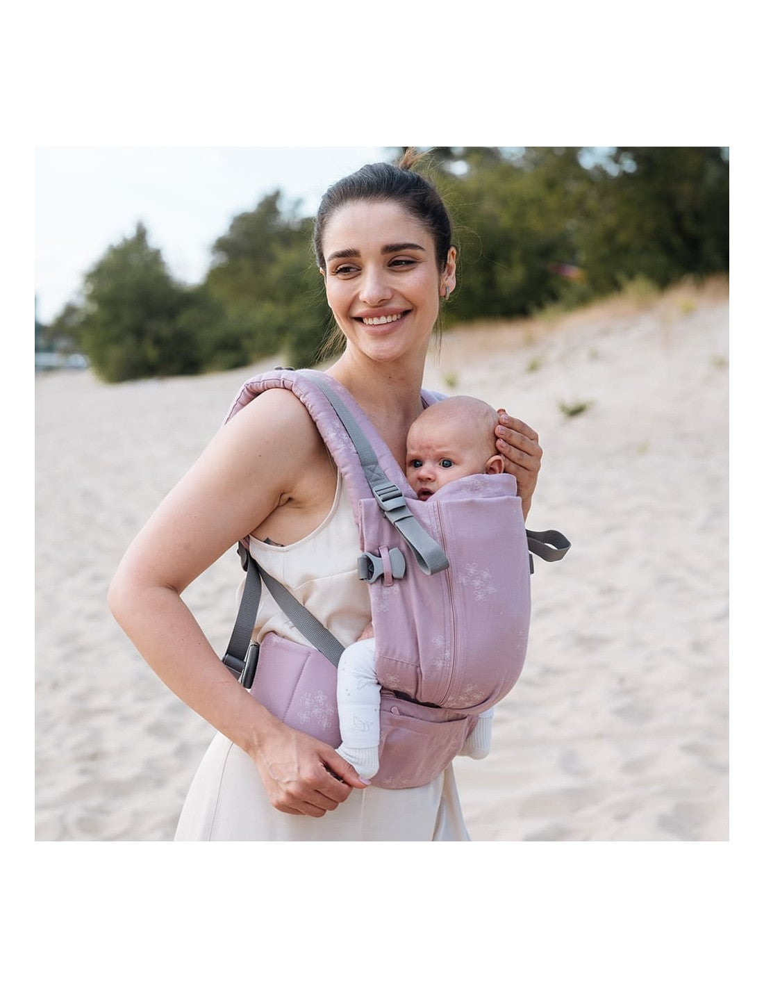 Mulher caminhando na praia com a mochila e o bebé, destacando a flexibilidade de uso.