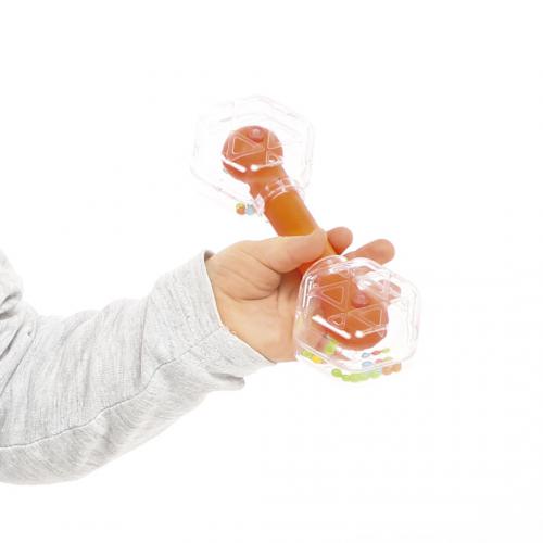 Mão de bebé a segurar o chocalho/maraca em forma de haltere, com contas coloridas visíveis no interior das extremidades transparentes.