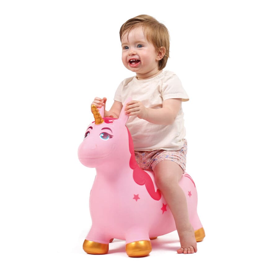Bebé sorridente a montar e a segurar as orelhas do unicórnio insuflável cor-de-rosa, ideal para brincadeiras ativas.