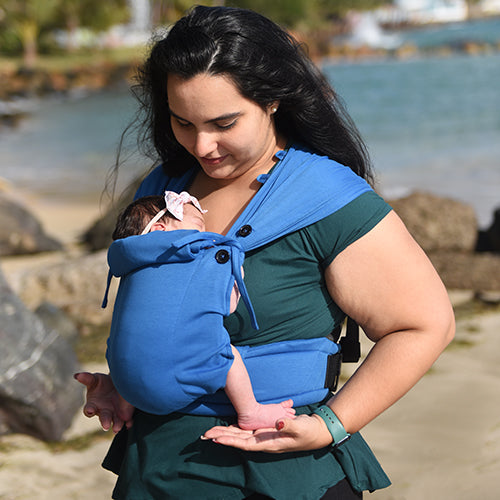 Mãe a olhar carinhosamente para o bebé recém-nascido na mochila de babywearing Neko Tiny cor azul, demonstrando o suporte.