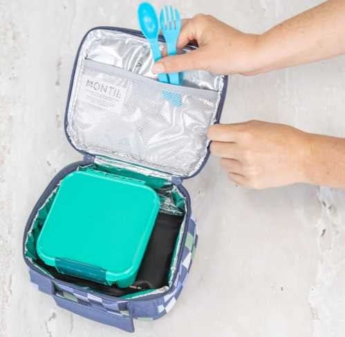 Mãos a colocar um recipiente de lanche verde-água e um bloco de gel dentro de uma bolsa de arrefecimento com padrão xadrez azul.