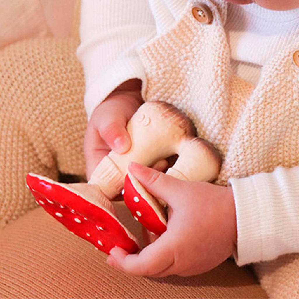 Mãos de um bebé a segurar o mordedor Spot o Cogumelo, mostrando o tamanho e a forma ergonómica do brinquedo.