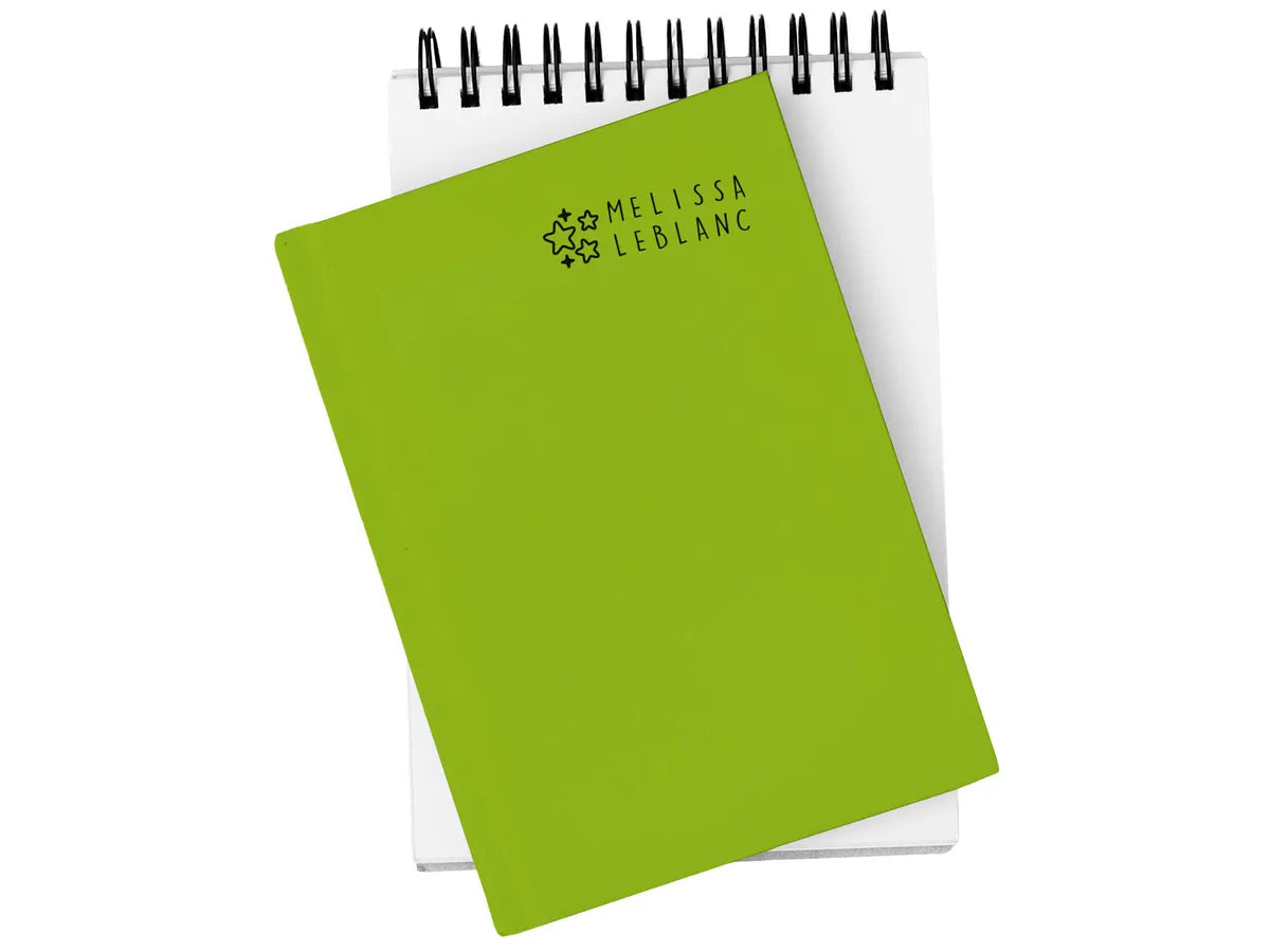 Demonstração do carimbo MARKY a personalizar a capa verde de um bloco de notas com o nome "MELISSA LEBLANC".