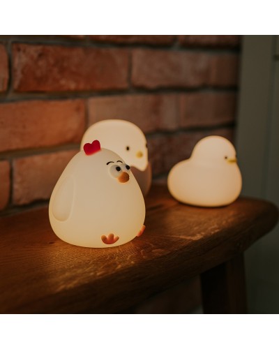 Luz noturna em forma de galinha de silicone branca, com detalhes em laranja nas patas e crista vermelha, iluminada com luz branca quente, ao lado de outras luzes noturnas em forma de animal.