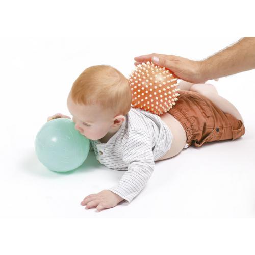 Mão de adulto a massajar as costas de um bebé com a bola sensorial Ludi.