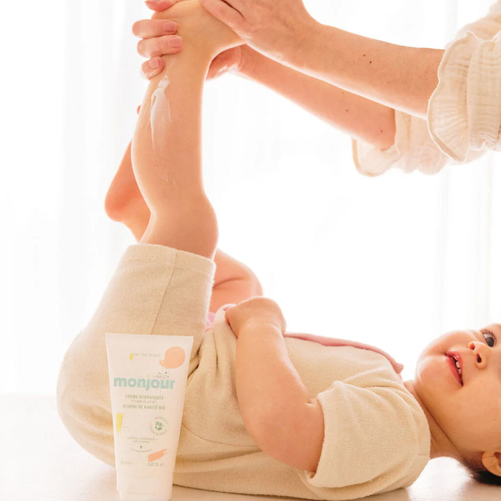 Bebé deitado a receber uma massagem hidratante nas pernas com o creme Monjour.
