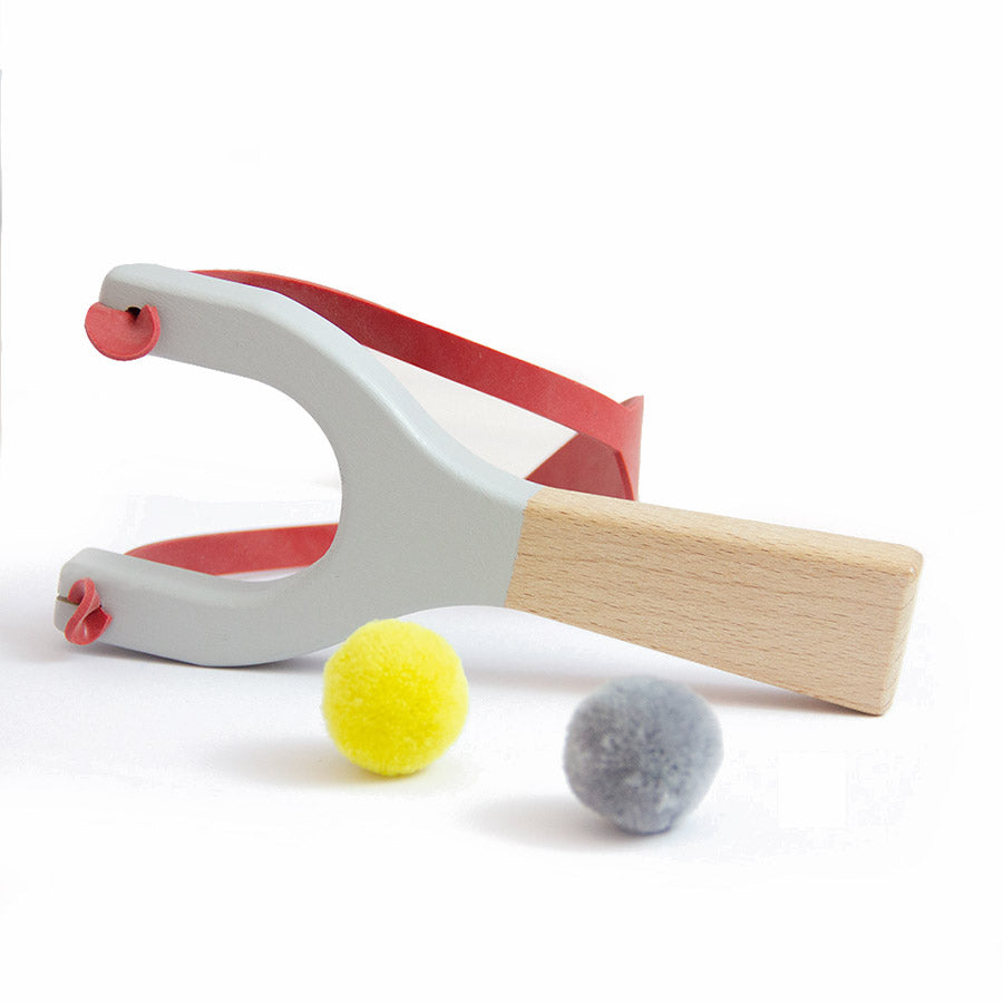 Detalhe da fisga Me & Mine mostrando a madeira polida e o elástico robusto, pintada com tintas ecológicas.