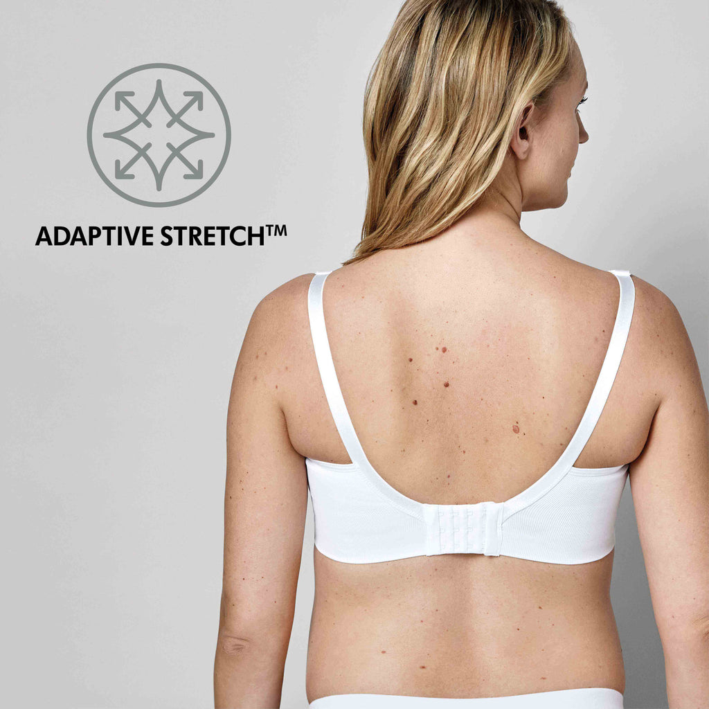 Vista traseira de mulher com sutiã Medela branco, mostrando o fecho de três filas de ganchos e o ícone "Adaptive Stretch" para elasticidade.