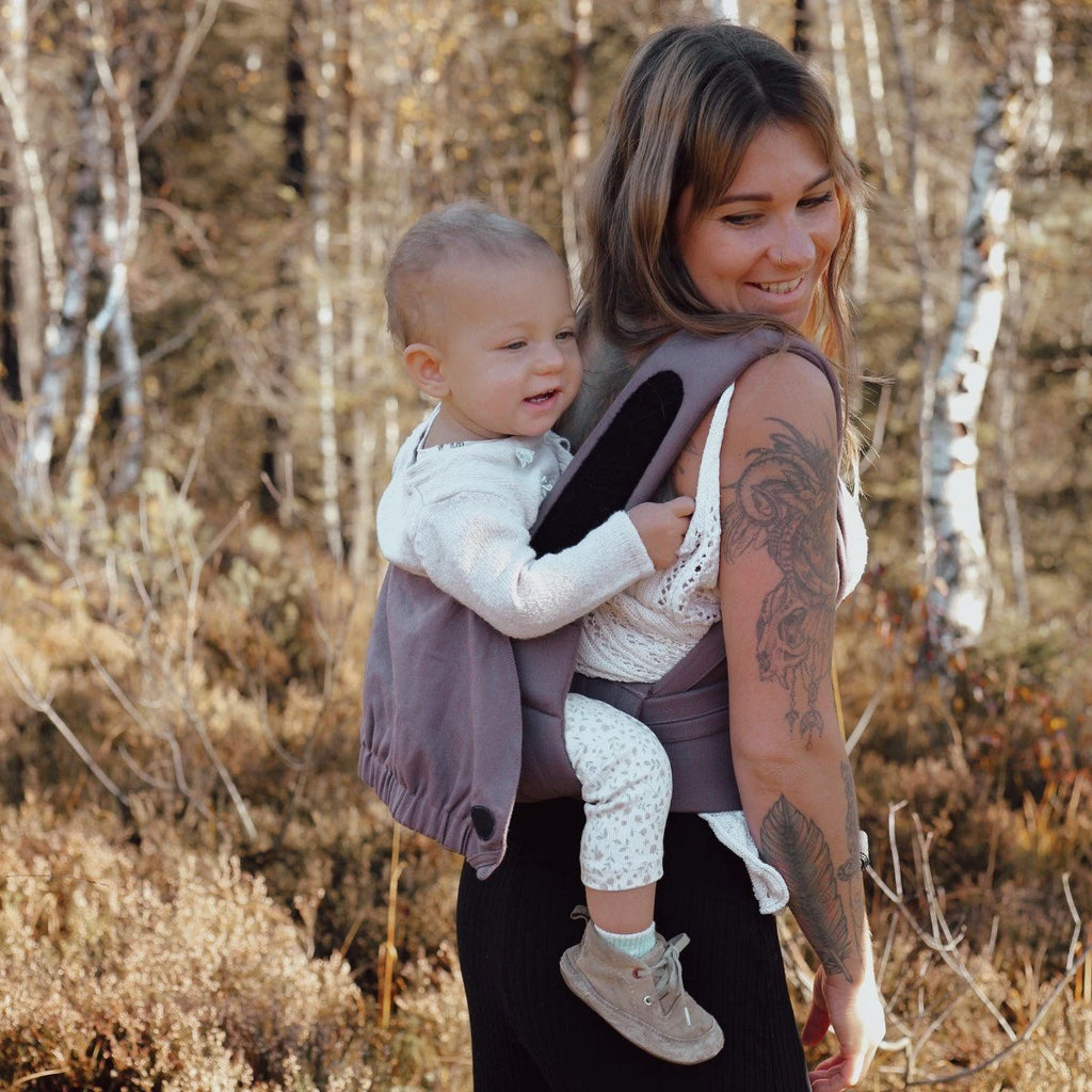Bebé transportado na posição frontal com o Mei Tai Hoppediz Bondolino B.Pure All Taupe, evidenciando a posição ergonómica em "M".