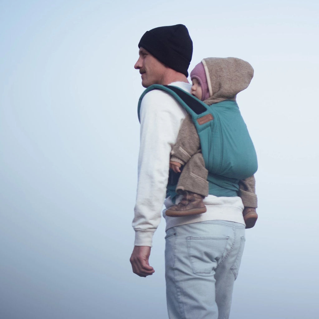 Vista traseira do Mei Tai Hoppediz Bondolino Plus Denim, mostrando o bebé seguro nas costas do cuidador com as alças atadas.