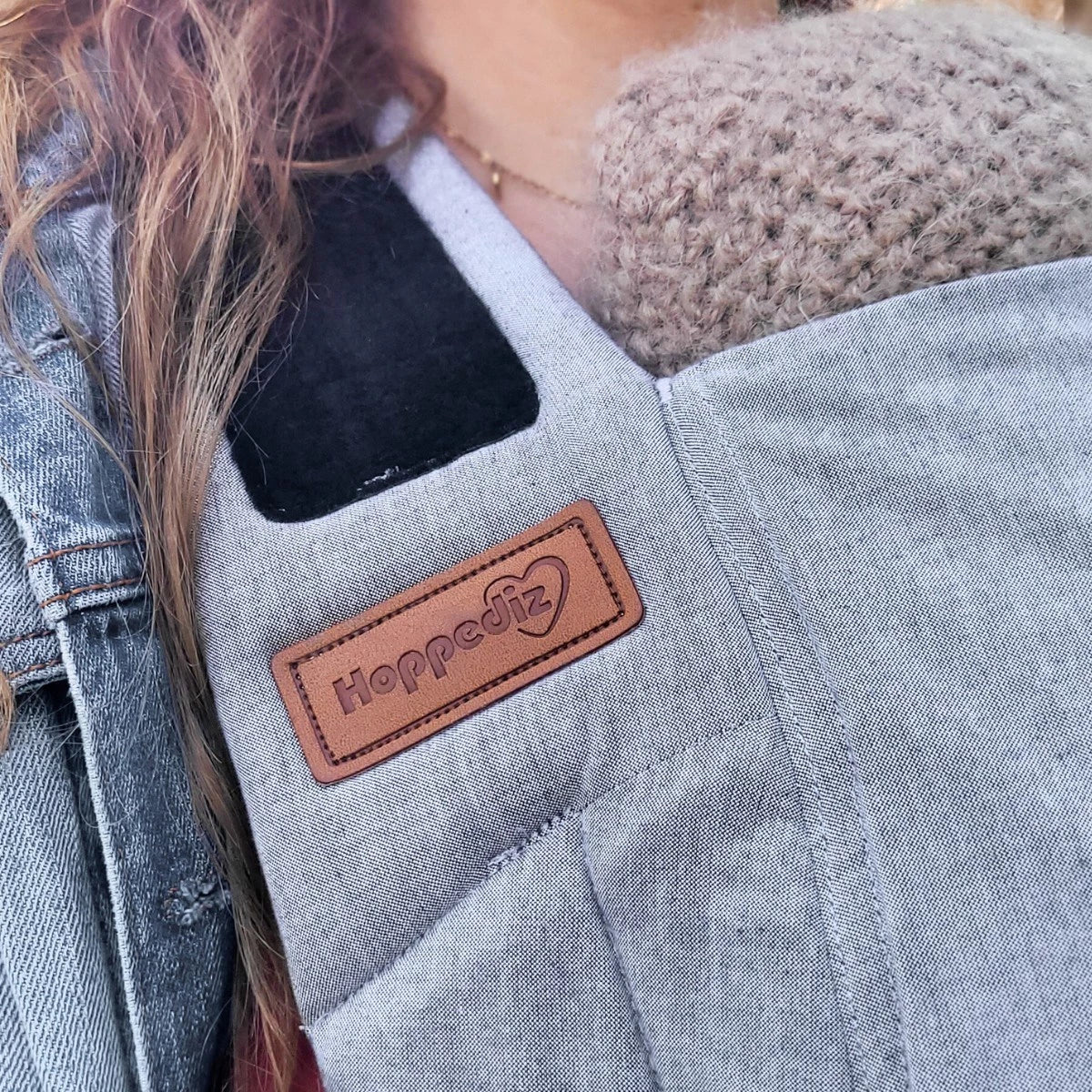 Bebé transportado na posição frontal com o Mei Tai Hoppediz Bondolino B.Pure All Grey, demonstrando o suporte ergonómico em "M" e a proximidade ao cuidador.