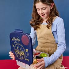 Menina a sorrir enquanto abre a sua lunchbox b.box Harry Potter, revelando as secções com fruta e lanches.