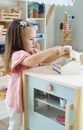 Uma menina brinca com a gelataria compacta de madeira small foot, servindo bolas de gelado com uma colher de madeira.