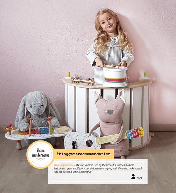 Uma menina a brincar com os instrumentos musicais small foot, incluindo os pauzinhos, num ambiente lúdico.