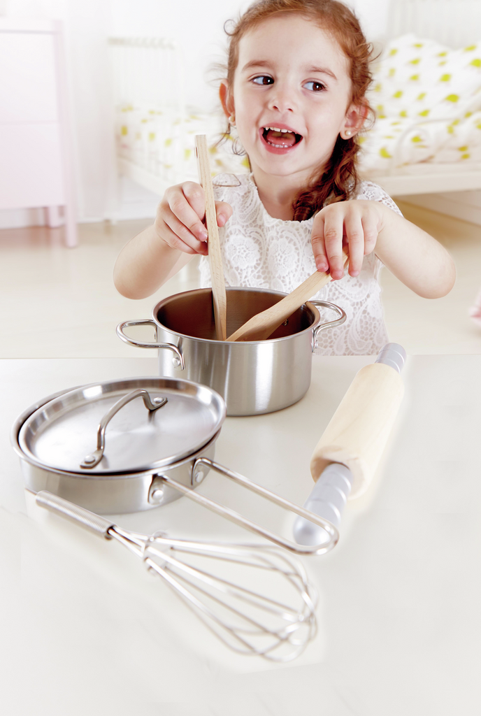 Menina sorridente a cozinhar com o set da Hape.