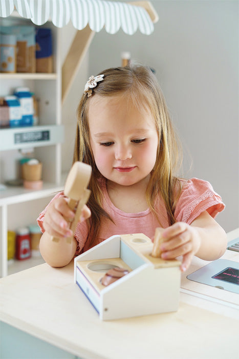 A menina concentra-se em colocar as bolas de gelado nos cones, mostrando a interação divertida com o brinquedo.