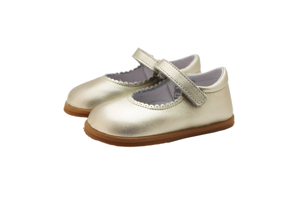 Merceditas Chloe em pele cor champagne, com fecho em Velcro e sola antiderrapante em borracha. Modelo clássico e elegante, ideal para cerimónia.